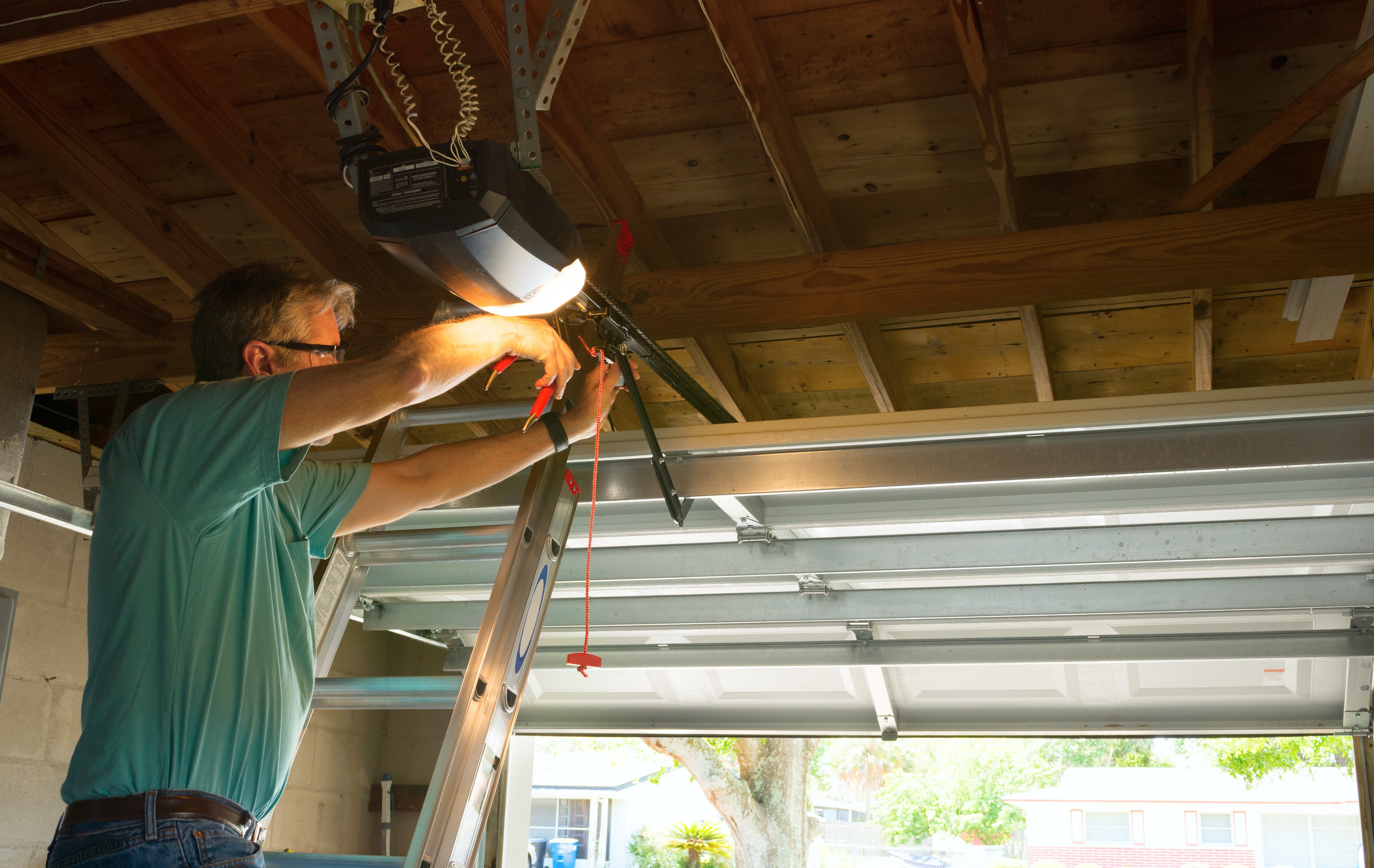 Image: A man repairing his garage door. Learn how to apply garage door lubricant. 